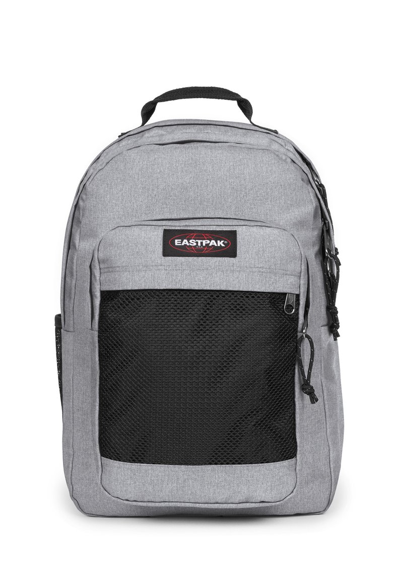 Grå nylonryggsäck med en svart mesh-fick framtill, handtag högst upp och justerbara axelremmar. Har en märkning med Eastpak-logotyp.