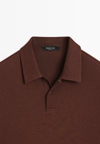 Brązowa koszulka polo wykonana z miękkiej mieszanki bawełny, z klasycznym kołnierzykiem, plisą na trzy guziki oraz subtelną fakturą dla dodatkowego efektu.