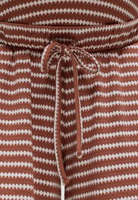 Πλεκτό παντελόνι με λευκές ζιγκ ζαγκ ρίγες σε σκουριασμένο φόντο, με αντίστοιχο κορδόνι δεμένο σε φιόγκο στη μέση.