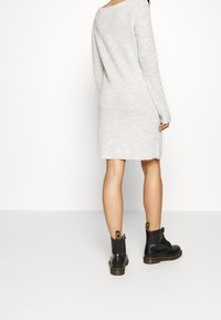 Stickad, långärmad, grå klänning med rundad halsringning, kombinerad med svarta snörkängor med gula hälflik. Enkelt och avslappnat snitt.