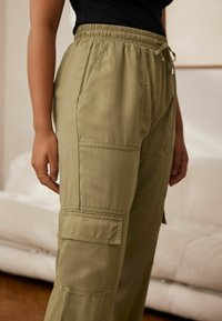 Groene cargobroek met een elastische tailleband, koordjes en meerdere zijzakken, met een gladde katoenmixtextuur.