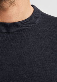 Ciemnoniebieski sweter wełniany z żebrowanym dekoltem typu crew, gładką teksturą i dopasowanym krojem, podkreślający szczegółowe ściegi wzdłuż krawędzi.