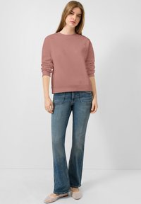 Stofroze sweatshirt met lange mouwen en ribgebreide manchetten, gecombineerd met lichtblauwe flared jeans en lichtgekleurde mesh instap schoenen.
