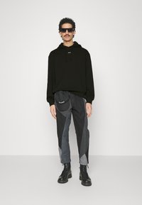Sudadera de algodón negra con cordones, combinada con pantalones gris y negro de patrón. El modelo lleva gafas de sol oscuras y botas negras de cordones.