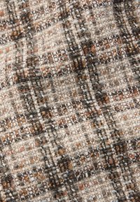 Kangas dengan pola tenun dalam nuansa beige, hitam, dan coklat. Memiliki permukaan yang lembut dan tekstur serta ketebalan benang yang bervariasi.