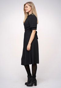 Fekete midi ruha rövid puffujjakkal, megkötős derékkal, fekete bokacsizmával és áttetsző fekete harisnyával párosítva.
