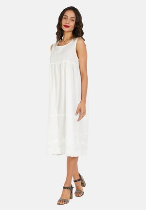 Vestido blanco sin mangas con escote redondeado, cintura fruncida y encaje en el dobladillo. Combinado con sandalias de tacón marrones.