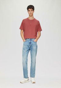 Rode kraagloze t-shirt met korte mouwen, lichtblauwe rechte jeans, witte sneakers met donkere accenten. Eenvoudig ontwerp met een casual uitstraling.