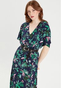 Blumenkleid in Marineblau mit grünen und pinken botanischen Mustern, mit V-Ausschnitt, kurzen Ärmeln und einem schwarzen Taillengürtel mit einer silbernen Schnalle.