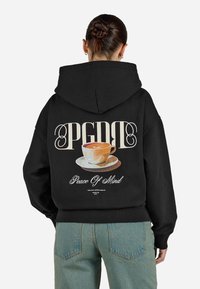 Felpa nera con cappuccio e grafica di una tazza di caffè sul retro, con testo decorativo "PGDR" e "Peace Of Mind" in colori a contrasto.