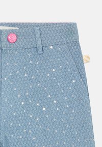 Lichtblauwe denim broek met een gestructureerd patroon, met pailletten en een roze glitters knoop in de taille. Accenten zijn een gouden label.