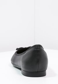 Ballerine noire avec un extérieur en cuir lisse, un bout rond, un talon bas et un bord élastiqué autour de l'ouverture. Pas de marquage visible.