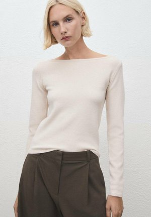 Suéter largo de color beige claro con escote barco, hecho de una tela suave, combinado con pantalones oscuros de tiro alto en tono marrón.