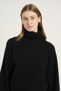 Pulover negru cu guler înalt, fabricat dintr-un tricot moale, texturat. Are un guler înalt și o croială ușor supradimensionată, cu mâneci raglan și cusături minime.