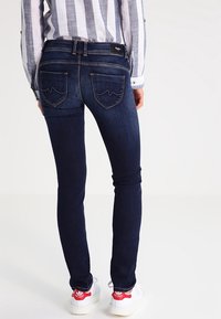 Mörkblå skinny jeans med en slät yta, med två bakfickor med böjd sömnad, ihop med vita sneakers.