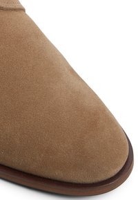 Hellbraune Wildlederschuhe mit runder Spitze, glatter Textur und einer kontrastierenden dunklen Holzsohle. Schlichtes Design ohne sichtbare Beschläge.