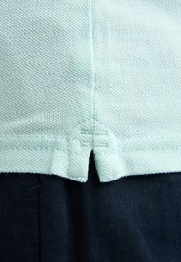 Licht muntgroene, gestructureerde stof met een split zoom ontwerp, zichtbare gestikte accenten, gecombineerd met donkere marineblauwe stof eronder.