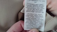Étiquette de soin textile sur un tissu beige indiquant la composition fibreuse, y compris "100 % Fibres Polyester - recyclées," en plusieurs langues.