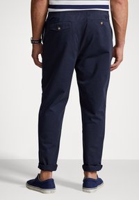 Granatowe bawełniane spodnie o luźnym kroju, z dwoma tylnymi kieszeniami i podwiniętymi nogawkami. Noszone z granatowymi wsuwanymi butami.