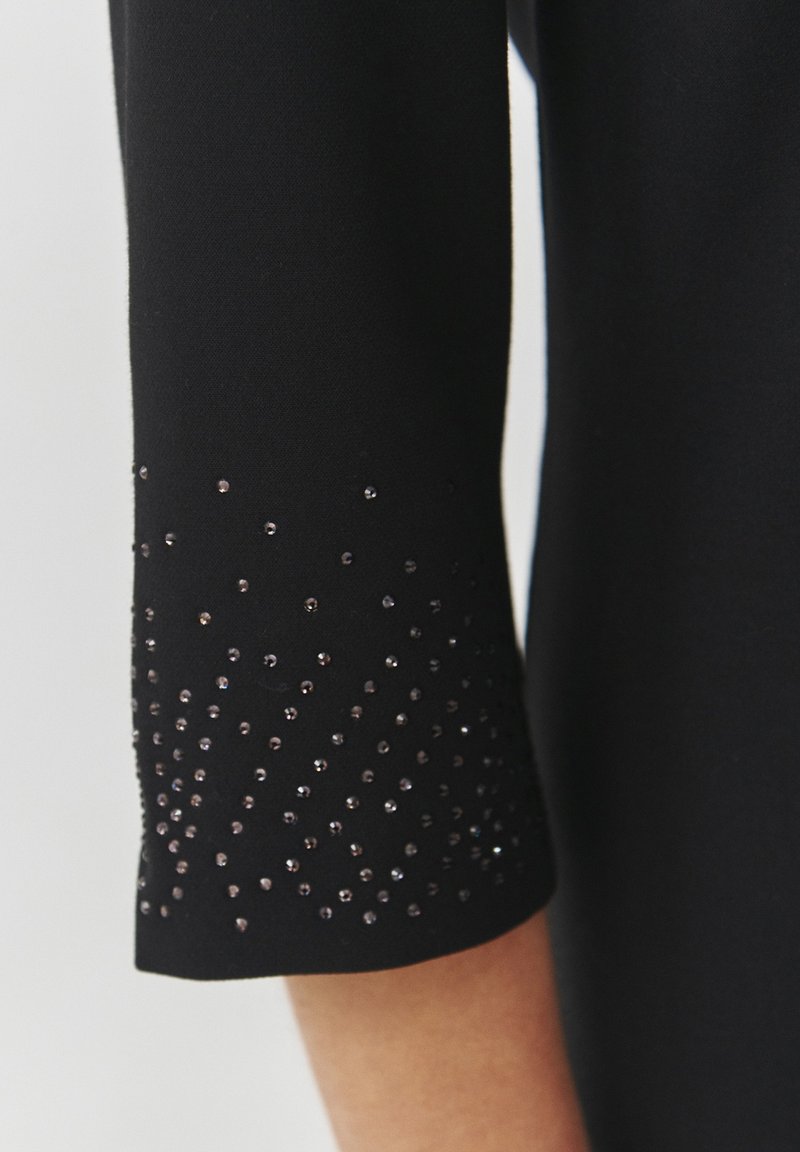 Czarna rękaw sukienki o gładkiej fakturze, z gradientem małych, lśniących koralików od łokcia do nadgarstka.