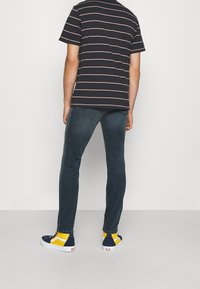 Marinrandig t-shirt med korta ärmar, tillsammans med mörka jeans. Avslutningen inkluderar strumpor med blå och gula mönster och blå sneakers.