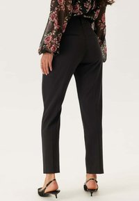 Zwarte op maat gemaakte broek met een slim fit, met een soepele textuur en subtiele achterzakken. Gecombineerd met een semi-doorzichtige bloes met bloemenmotief.