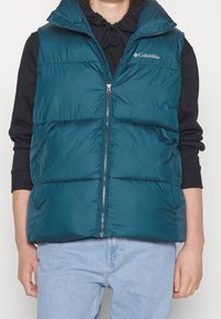 Tiefblaues Puffer-Weste mit Reißverschluss und Kapuze, ausgestattet mit horizontalen Steppabschnitten. Das Material ist sauber und glänzend, mit Columbia-Logo versehen.