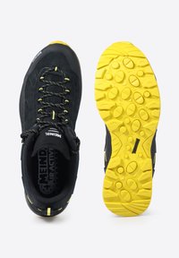 Scarpa da trekking nera con tomaia testurizzata, lacci gialli e suola in gomma con un motivo a multifunzione. Logo visibile sulla linguetta.