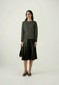 Sweater cinza texturizado com bainha canelada, combinado com uma saia midi de couro preta. Mulher segurando uma mala preta e usando saltos abertos pretos.