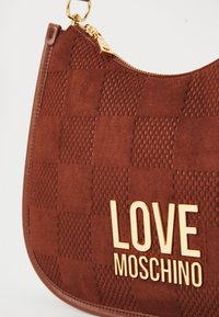 Braune Wildleder-Handtasche mit geprägtem Schachbrettmuster, goldenem Reißverschluss und goldenem "LOVE MOSCHINO"-Logo auf der Vorderseite.