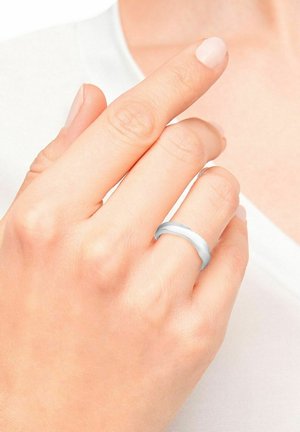 Bague en argent à finition lisse portée à un doigt. Elle présente un design simple et arrondi avec une surface brillante, contrastant avec un teint de peau clair.