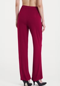 Pantaloni larghi rossi con una texture liscia, vita elastica e due tasche laterali, abbinati a scarpe nere con tacchi alti.