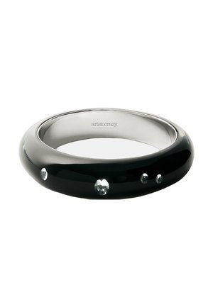 Brazalete negro pulido con cuatro piedras preciosas claras incrustadas y la palabra "aristocrazy" grabada en el interior.