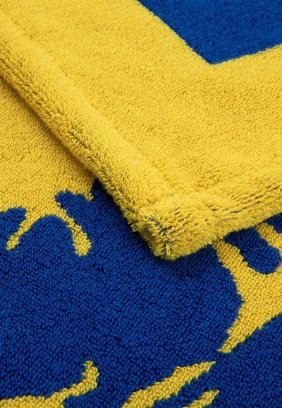 Κίτρινο και μπλε υφασμάτινο ύφασμα με γωνία διπλωμένη, που δείχνει ένα έντονο, αφηρημένο μοτίβο και υλικό από λουρίδες πετσέτας.
