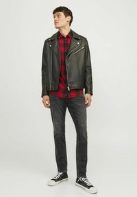 Chaqueta de cuero negra de motorista, camisa de cuadros roja y negra, jeans oscuros y zapatillas negras con suelas blancas. La chaqueta cuenta con herrajes plateados.