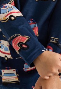 Granatowa koszula z długim rękawem z nadrukiem w wózki strażackie i ambulanse. Tkanina jest miękka o gładkiej fakturze; detale w kolorze czerwonym i białym.