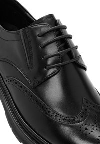 Zwarte leren dress shoe met een ronde neus, vetersluiting, wingtip-details, brogue-perforaties en een dikke zool.