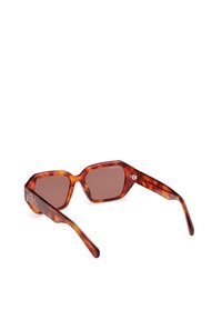 Ochelari de soare tortoise brown cu o formă hexagonală, lentile căprii și laterale texturate. Prezintă un detaliu subtil cu logo pe bradă.