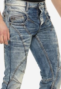 Jeans de mezclilla azul deslavada con un acabado texturizado, que cuentan con costuras decorativas, un bolsillo con cremallera y diseños de paneles distintivos.