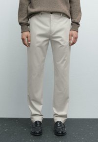 Beige trousers with straight-leg design, cotton material, side pockets, and a smooth texture, paired with black loafers.