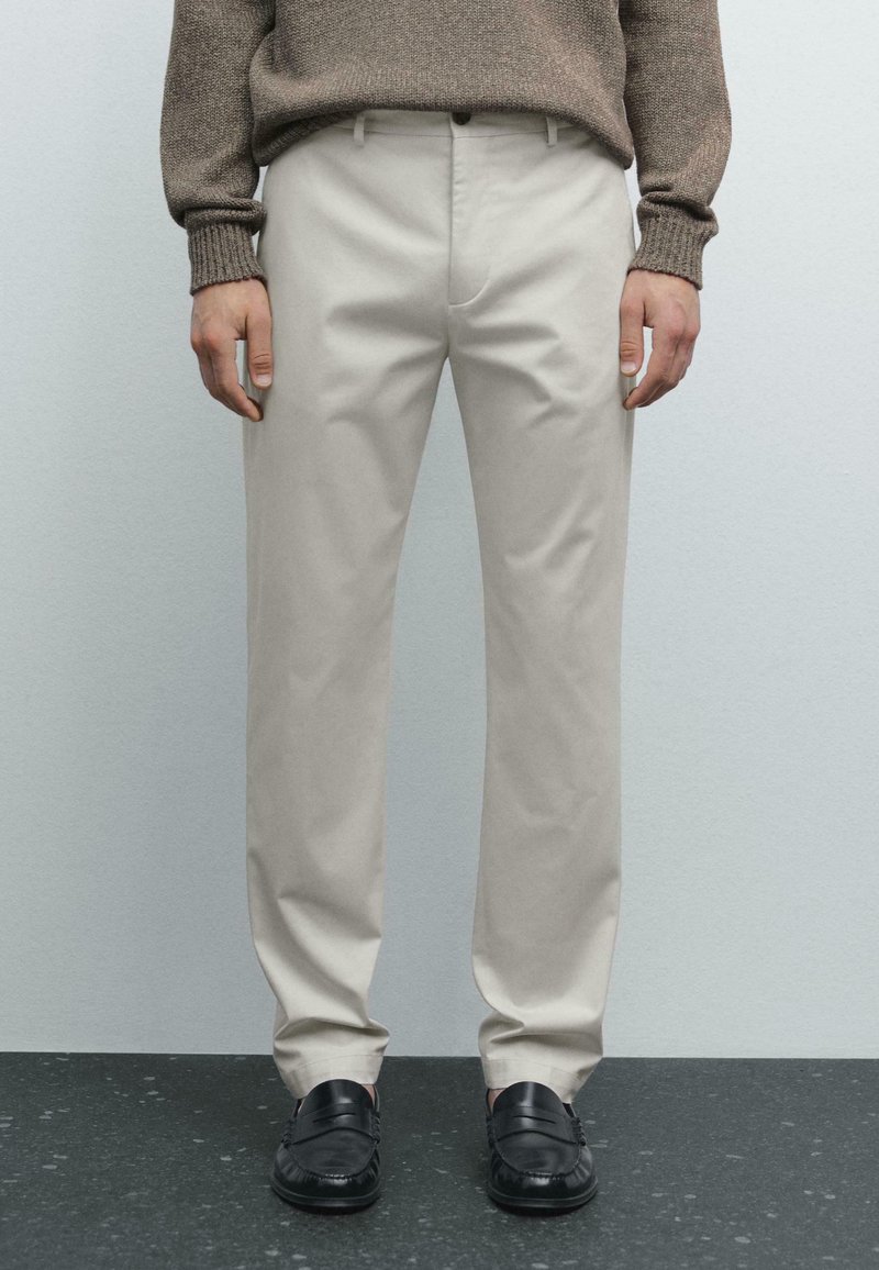 Beige trousers with straight-leg design, cotton material, side pockets, and a smooth texture, paired with black loafers.