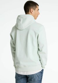 Sudadera verde claro con una textura suave, capucha con cordón y puños acanalados. Combinada con jeans azules, que presentan un ajuste y diseño relajados.