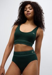Σετ με σκούρο πράσινο ριμπ μπραλέ και εσώρουχα με ψηλή μέση και λεπτομέρειες με λογότυπο. Το ύφασμα έχει λεία υφή και εφαρμοστή σχεδίαση.
