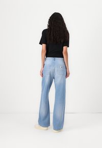Ljusblå vida jeans med hög midja, bakfickor och en liten logotypapplikation. Bärs med en svart t-shirt med kort ärm och vita skor.