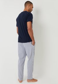 T-shirt in cotone navy abbinato a pantaloni del pigiama a righe, comodi e rilassati, con tasche laterali e tessuto leggero. Modello a piedi nudi visto da dietro.