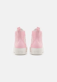 Pár růžových vysokých tenisek Converse zobrazených z pohledu zezadu na bílém pozadí, s bílými gumovými podrážkami a logy na patě.