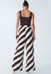 Brown tank top paired with wide-leg trousers featuring bold brown and white diagonal stripes. Elastic waistband and lightweight fabric.
