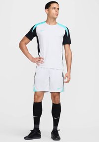 Conjunto deportivo de Nike que incluye una camiseta de manga corta blanca y negra con detalles en turquesa, combinada con pantalones cortos a juego y calcetas negras.