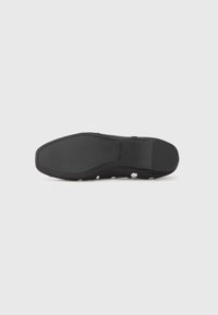 Suela de zapato de goma negra con diseño plano, con tachuelas circulares plateadas en el lateral. Parte inferior texturizada para mayor agarre.