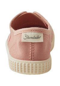 Light pink canvas shoe featuring a soft fabric upper, white rubber sole, and a label stitched on the heel. Rounded back design.